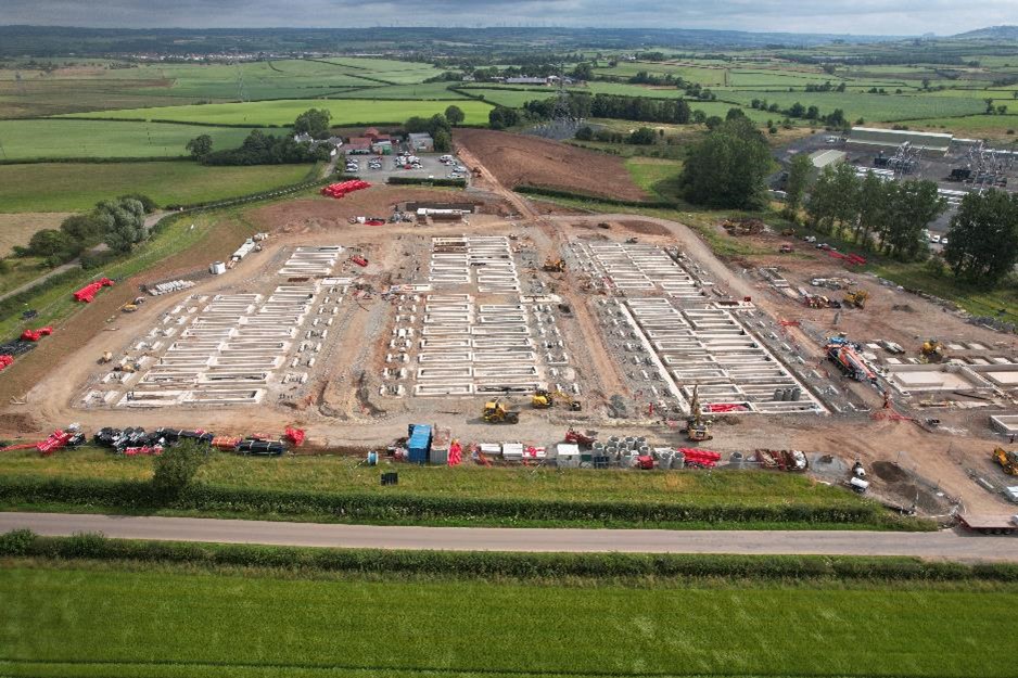 Aerial view of Kilmarnock South BESS site with battery foundations, construction equipment, and surrounding green fields.