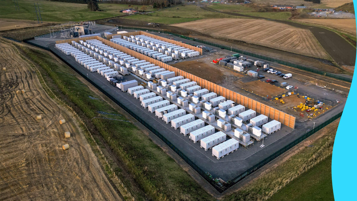 Aerial view of Zenobē’s Blackhillock battery storage site, showcasing rows of white battery containers, wooden wind breaker panels, and surrounding green fields.