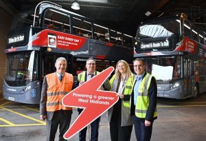 Four people wearing high viz standing in front of two new electric buses