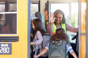 As her riders board the school bus, a female bus driver high-fives them from the driver's seat.